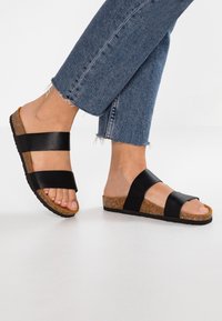 Sandali scivolati in pelle nera con due ampie cinghie e suola in sughero testurizzato, abbinati a jeans in denim blu a culotte con orli sfrangiati.