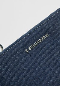 Denimowy worek w ciemnoniebieskim kolorze z metalowymi elementami w srebrnym odcieniu i przeszyciami; posiada naszywkę z logo "Stradivarius". Płaska konstrukcja z fakturowaną powierzchnią.