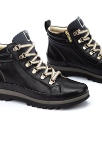 Bottines noires en cuir avec des lacets beiges, des accents en métal doré, un panneau texturé gris et une fermeture éclair sur le côté.