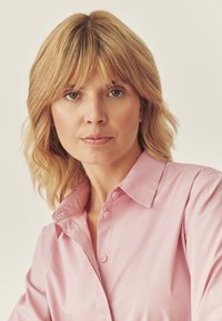 Jasnoróżowa koszula na guziki z kołnierzykiem, o gładkiej fakturze i casualowym kroju, wyeksponowana na neutralnym tle.