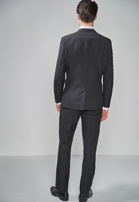 Chaqueta y pantalones negros con un corte a medida, textura suave y solapas con muesca, combinados con una camisa blanca y zapatos negros.
