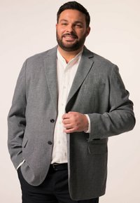 Szary żakiet o teksturowanej powierzchni, zapinany na dwa czarne guziki, noszony na białej koszuli. Żakiet ma pojedynczą kieszeń na piersi oraz dopasowany krój.