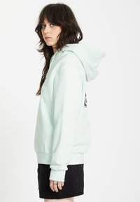 Felpa con cappuccio verde menta, dotata di tasca a marsupio, polsini e orlo a coste, indossata con una gonna in denim nera, caratterizzata da dettagli di cucitura visibili.