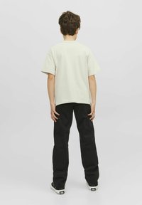 Ljusbeige oversized t-shirt med korta ärmar. Bärs med svarta vida byxor, vilket visar en enkel design utan synliga logotyper eller mönster.