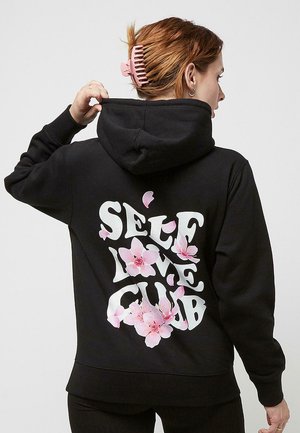 Musta huppari, jossa on valkoinen teksti "SELF LOVE CLUB" pinkeillä kukka-yksityiskohdilla. Materiaali on puuvillasekoitetta ja malli on rento.