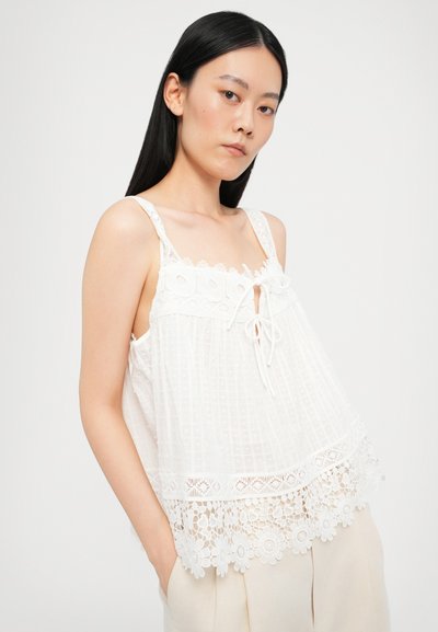 White sleeveless top with textured fabric, lace trim, and decorative lace hem. Features a tie detail at the neckline.