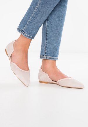 Light pink suede flats with pointed toe, cut-out sides, and a minimal beige sole, paired with blue denim jeans.