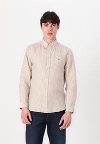 Camisa de hombre de manga larga en beige con finas rayas verticales blancas. Cuenta con cuello abotonado y un pequeño logo en el bolsillo del pecho.