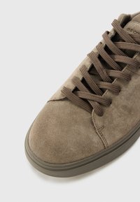 Baskets en daim marron avec bout rond, tige texturée et lacets ton sur ton. Présente une semelle extérieure en caoutchouc solide et un design minimaliste.