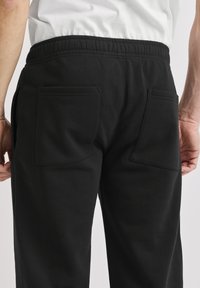 Schwarze Jogginghosen mit lockerer Passform, elastischem Bund, zwei Gesäßtaschen mit sauberer Naht und weicher Textur.