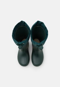 Bottes en caoutchouc vertes avec un col en tissu doux en haut, dotées d'un accent de bouton et d'une texture lisse et brillante.