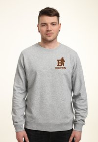 Felpa grigia realizzata in misto cotone, con un logo marrone che mostra un orso e la parola "BROWN" sul lato sinistro del petto. Collo a giroclassico.