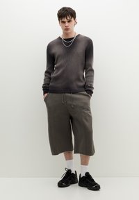Grijze geribbelde trui met een donkere gradient, gecombineerd met losse grijze cargoshorts. Zwarte sneakers en witte sokken maken de look af.