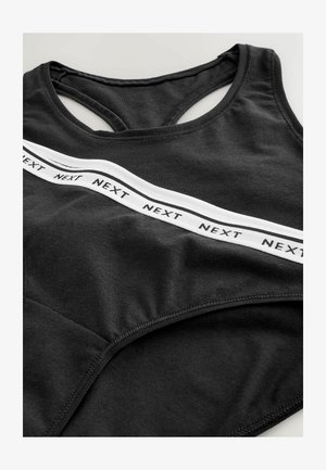 Fekete sportmelltartó, hátul versenypályára tervezett kialakítással, puha pamut anyagból, és egy fehér pánttal, amelyen az "NEXT" szó ismétlődik az elején.