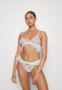 Conjunto de lingerie de renda branca composto por um bralette com alças ajustáveis e detalhes em recorte, acompanhado de uma lingerie de cintura alta combinando, decorada com bordas em forma de onda.