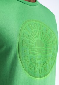 Camiseta de algodón verde con un gran logotipo en relieve tono sobre tono, con cuello redondo y mangas cortas. Tejido suave y de peso medio.