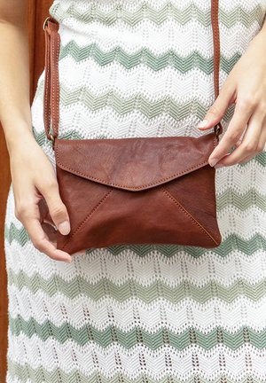 Ruda odinė per petį nešiojama rankinė su užlenkiamu dizainu, lygiu paviršiumi ir trikampiais akcentais apačioje. Prisegta dirželiai nešiojimui.