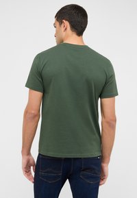 Zielona bawełniana koszulka z krótkim rękawem i okrągłym dekoltem, o gładkiej fakturze i jednolitym wzorze, zestawiona z ciemnymi dżinsami.