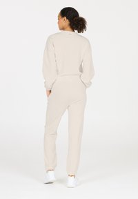 Beige Sweatshirt und passende Jogginghose aus weichem Stoff mit elastischen Bündchen und Bund, mit minimaler Markenkennzeichnung am Kragen.