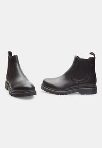 Bottines en cuir noir avec panneaux élastiques sur les côtés, bout rond et semelle en caoutchouc texturée. Possède une languette à l'arrière.