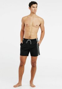 Zwarte zwembroek met een grijze trekkoord, voorzien van een zijlogo print. Gemaakt van lichtgewicht materiaal, korte lengte en met zakken aan de zijkanten.