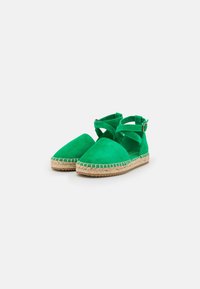 Gröna mocka espadrillos med en vävd jute-sula, med korsande remmar och en rund accentknapp på sidan.