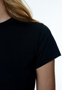 Schwarzes Baumwoll-T-Shirt mit kurzen Ärmeln und rundem Ausschnitt, das eine glatte Textur und saubere Nähte aufweist.