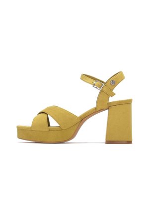 Sandalias de tacón de ante amarillo con diseño de tiras cruzadas, correa ajustable en el tobillo y tacón grueso de bloque, con una superficie texturizada.