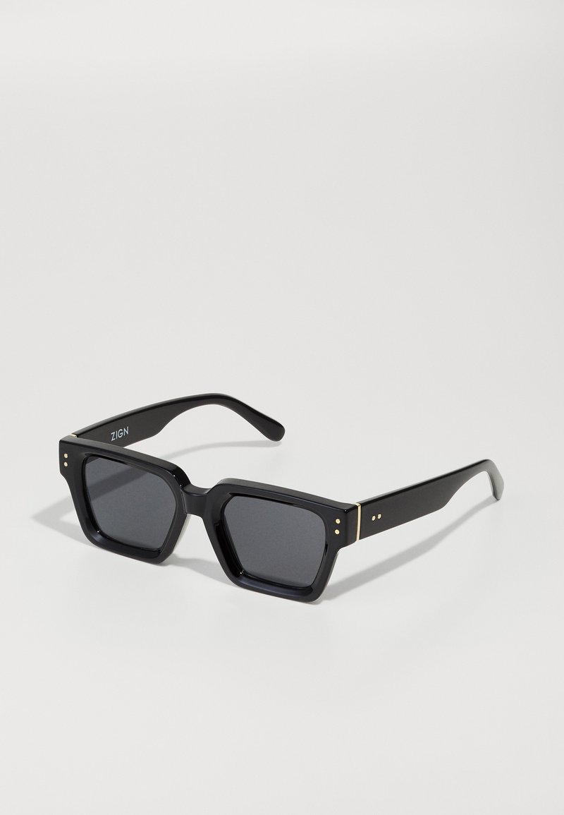Óculos de sol quadrados pretos com lentes escuras. Feitos de plástico brilhante, com detalhes em dourado na armação e três pequenos pontos perto das dobradiças.
