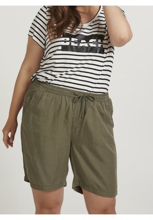 Kobieta ubrana w oliwkowo-zielone szorty ze sznurkiem i czarno-biały pasiassty T-shirt z napisem "BEACH" na przodzie, pozująca na jednolitym tle.