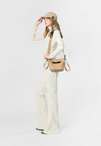 Bolso cruzado de cuero beige con textura suave, correa ajustable y cierre de cremallera. Combinado con una blusa color crema y pantalones de pierna ancha.
