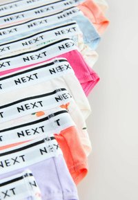 Pile de sous-vêtements colorés pour enfants avec des ceintures élastiques blanches étiquetées « NEXT » sur un fond clair.
