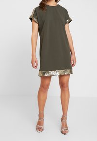 Oliwkowa bawełniana sukienka z krótkimi rękawami, z złotymi cekinami na rękawach i u dołu, w luźnym kroju.