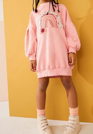 Robe sweat rose avec des manches ballons, ornée de broderies arc-en-ciel et de fleurs avec des sequins. Détail d'ourlet à volants, associée à des baskets montantes.