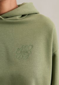 Felpa verde in cotone con vestibilità comoda, caratterizzata da un tessuto testurizzato, un ampio cappuccio e un logo in rilievo sul petto.