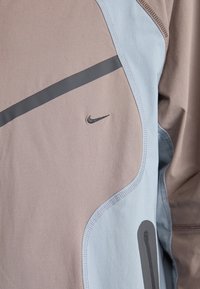 Nike sports top med et design i lys brun og blå, blødt stof, buede sømme og et lille broderet logo i sort.