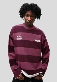 Maroon and purple striped long-sleeve sweatshirt with a crew neckline and printed logos. Features a raw hem and soft texture.