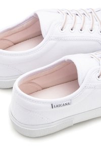White canvas sneakers with a rubber sole, featuring light pink interior lining, round toe, and lace-up design with beige laces.