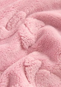 Mjuk rosa fleecefilt med en texturerad, plyschyta. Tyget har ett mysigt, vågformat mönster och en fluffig känsla.
