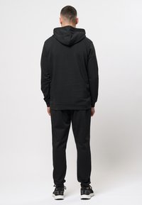 Zwarte hoodie en bijpassende sweatpants van zachte stof. Bevat een capuchon met trekkoord en elastische manchetten, met een effen kleur overal.