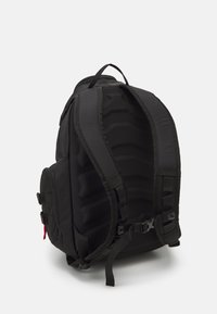 Black backpack with padded back panel, adjustable straps, and side zipper pocket. Features textured fabric and adjustable buckle closure.