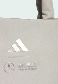 Grå stofnettaske med en tekstureret yderside, præget hvidt Adidas-logo og sølvfarvet Mercedes-Benz AMG Petronas-mærkning.