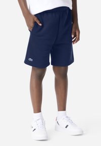 Marineblauwe sportshorts met een elastische tailleband, zijzakken en een klein wit geborduurd logo op de linkeronderzoom.