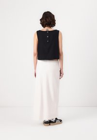 Svart cropped ermeløs topp med knappedetalj på baksiden, brukt med et langt hvitt skjørt og svarte sneakers. Enkel design, glatt tekstur.