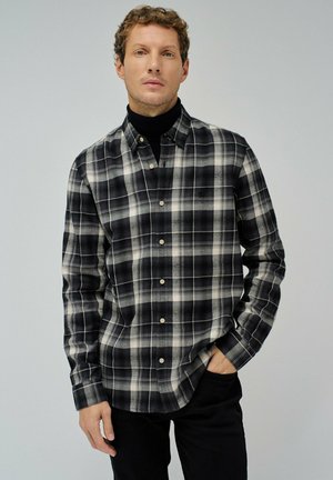 Camisa de franela a cuadros en blanco y negro con cuello, presenta botones en la parte delantera y mangas largas, combinada con un suéter de cuello alto negro.