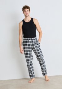Débardeur noir et pantalon de pyjama à carreaux gris avec une taille élastique, affichant une coupe décontractée et un motif à carreaux, modèle debout pieds nus.