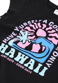 Camiseta de tirantes negra de algodón con un diseño gráfico colorido: texto en rosa y azul con motivos de palmera, ola y sol. El texto dice "HAWAII."