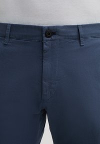 Pantaloni blu navy con tessuto strutturato, dotati di chiusura frontale con bottone, tasche laterali angolate e design slim fit.