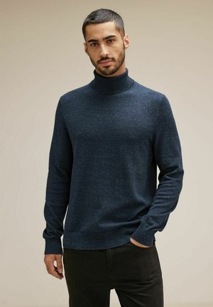 Suéter de cuello alto azul marino con un acabado texturizado, que cuenta con mangas largas y un diseño ajustado. Llevado con pantalones negros.