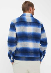 Camicia button-up in un motivo a quadri blu e bianchi, con tessuto testurizzato, maniche lunghe e colletto. Presenta cuciture e bottoni in evidenza.